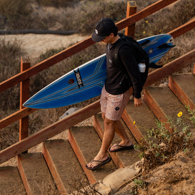 A man walking down sandy steps at the beach wearing Cobian Compass Chocolate Sandals #color_chocolate