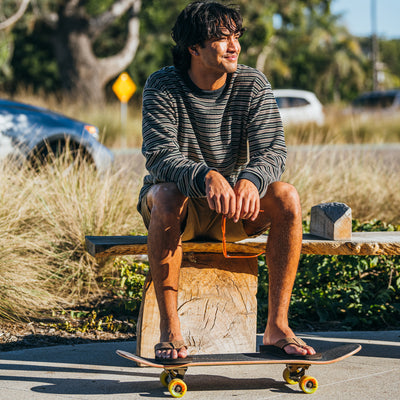 A man sitting on a bench resting his feet on a skateboard wearing the Cobian® Floater 2™ Mocha sandals #color_mocha