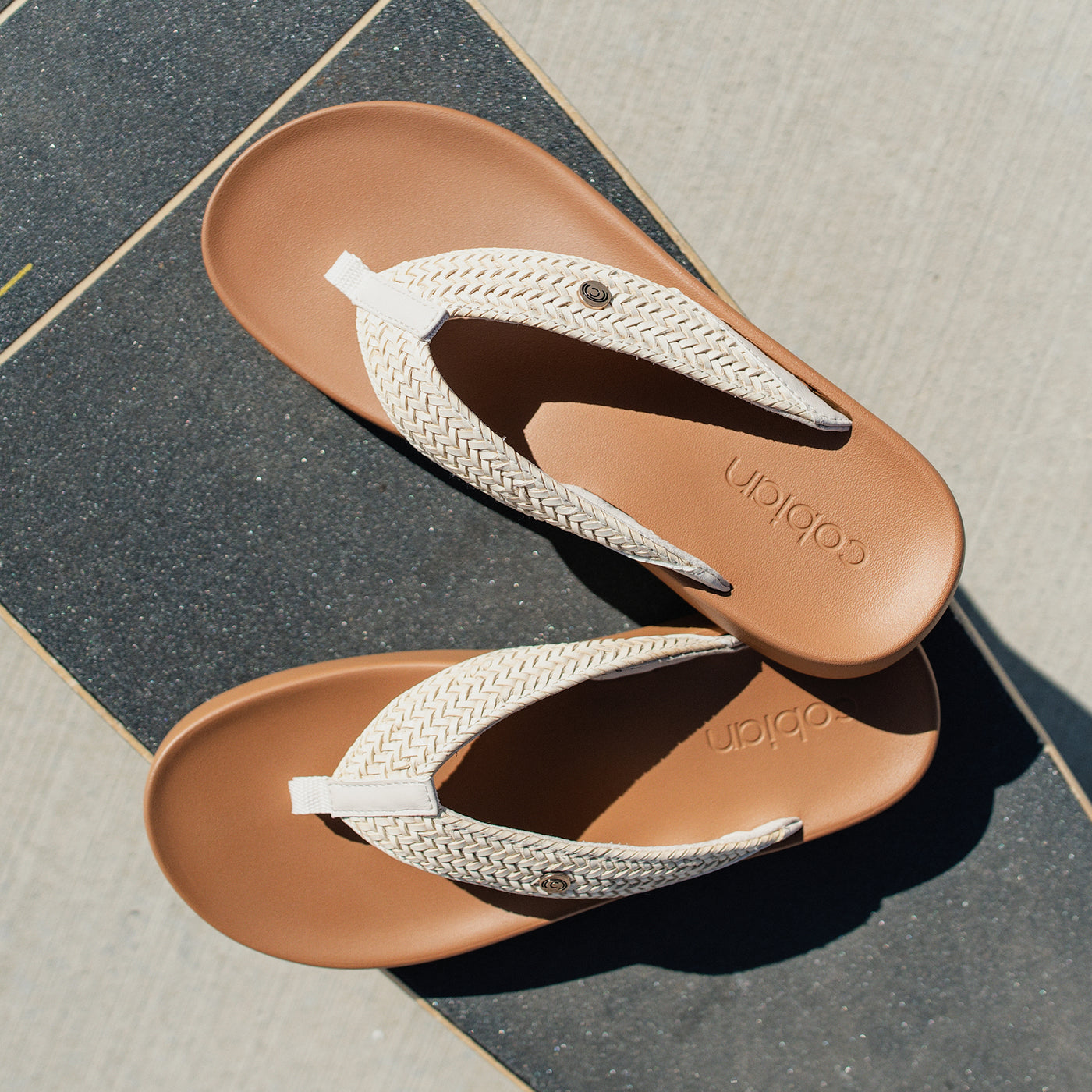 A close up the Cobian Palmilla Cream sandals on a skateboard deck #color_cream